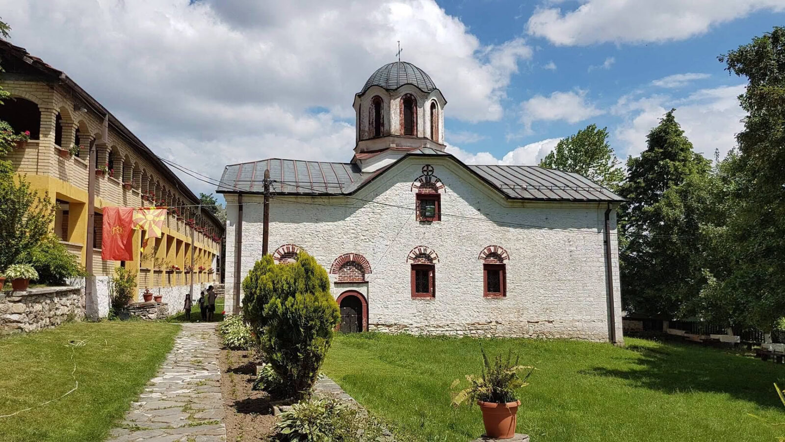 A historic whitewashed church with a domed bell tower in a green courtyard